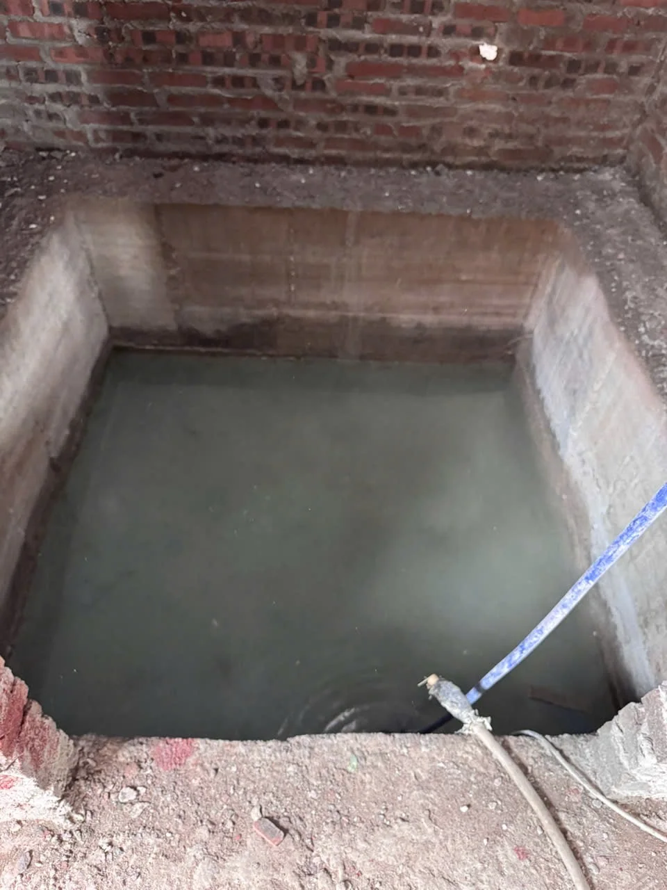 Hố pit trong nền nhà thô, đáy có bề mặt nước và vật liệu thi công.