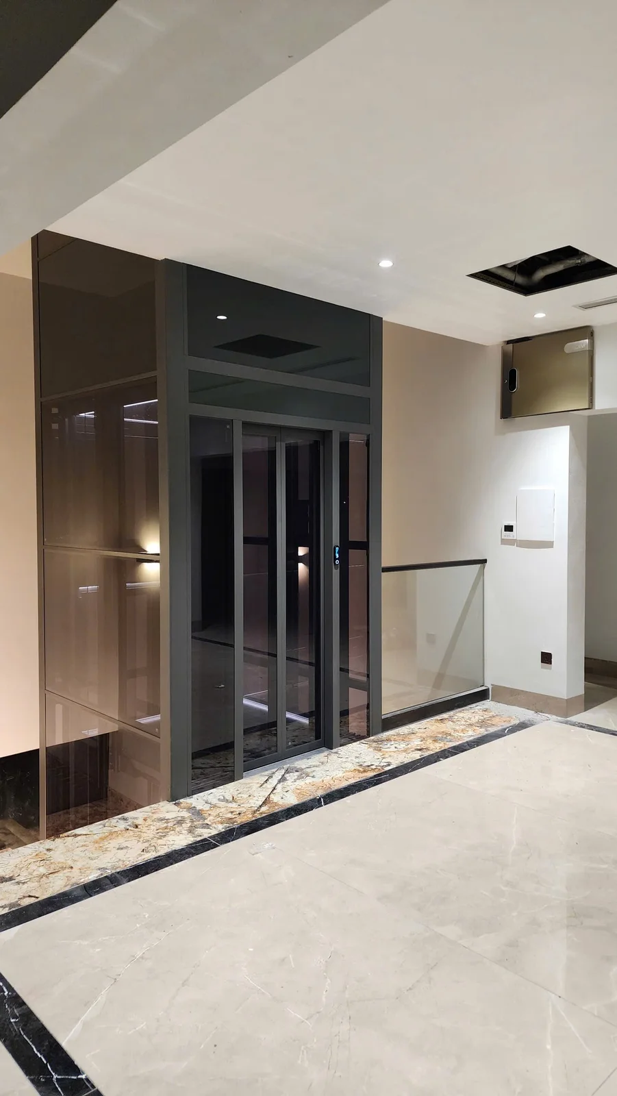Thang kính khung tối tại khoảng chiếu nghỉ cạnh lan can kính.