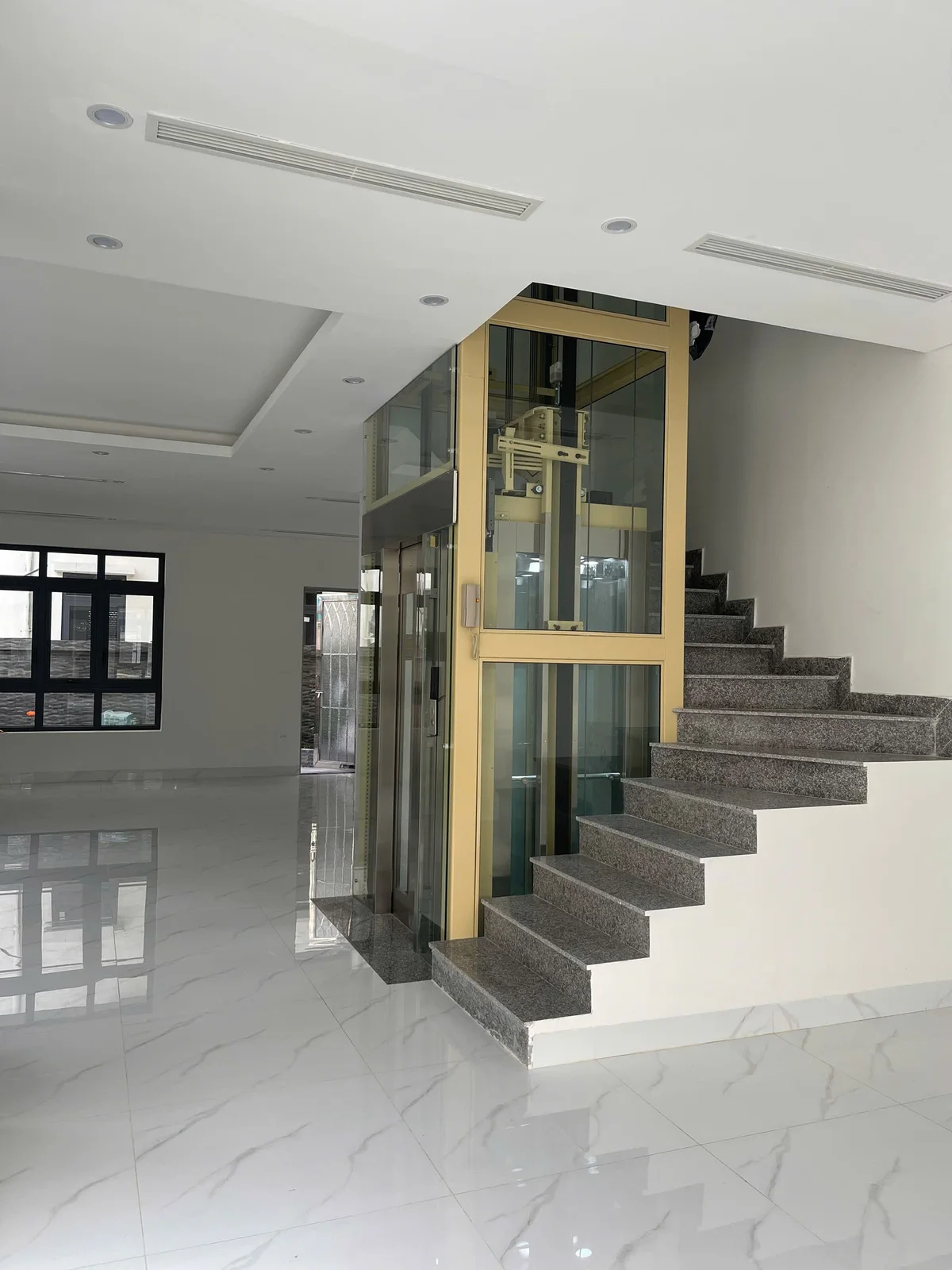Khung và vách kính màu vàng cạnh cầu thang đá trong sảnh trắng.