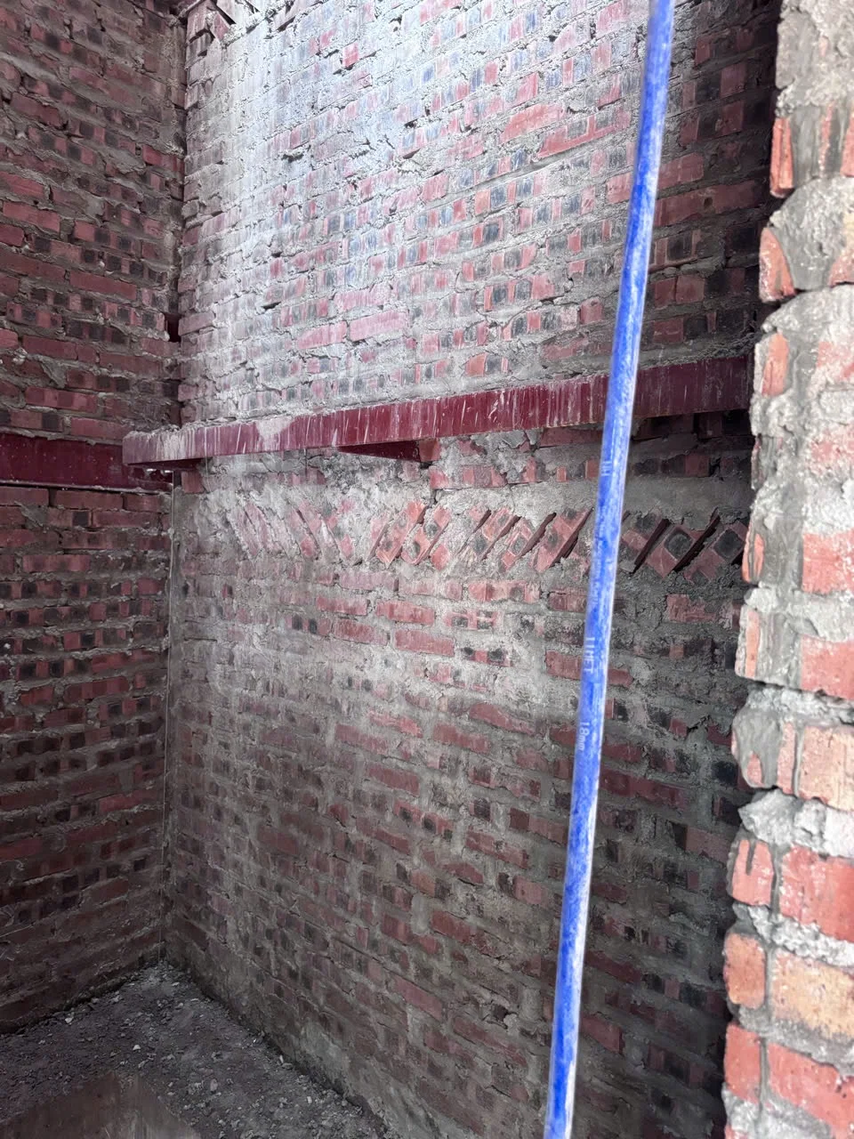 Khoang giếng thang tường gạch thô, có dầm ngang và thanh đứng.