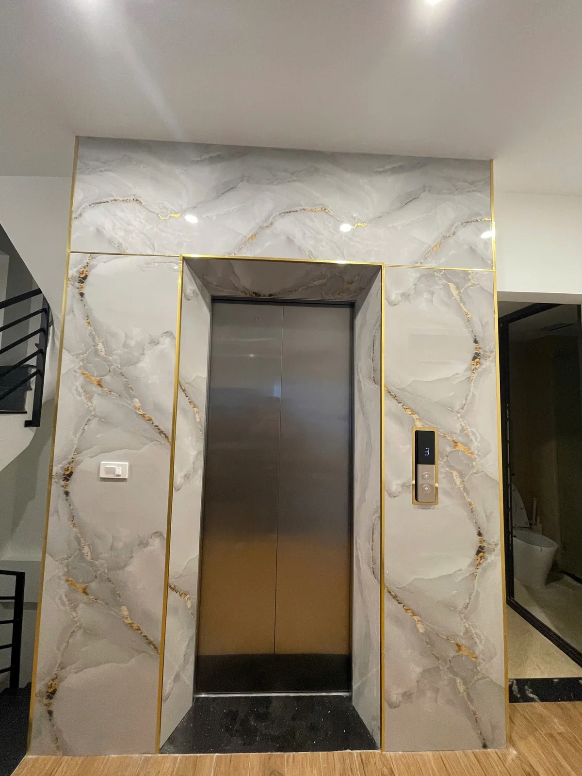 Mặt cửa thang inox đóng trong mảng đá sáng vân vàng.