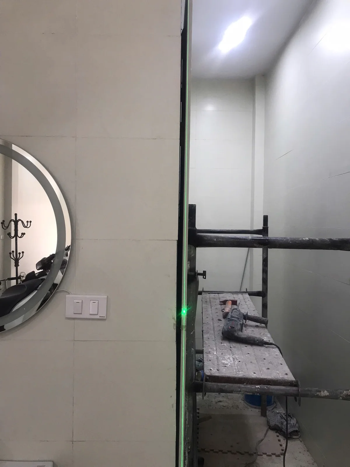 Khu vực cửa và giàn giáo đang thi công, có vệt sáng laser trên cạnh khung.