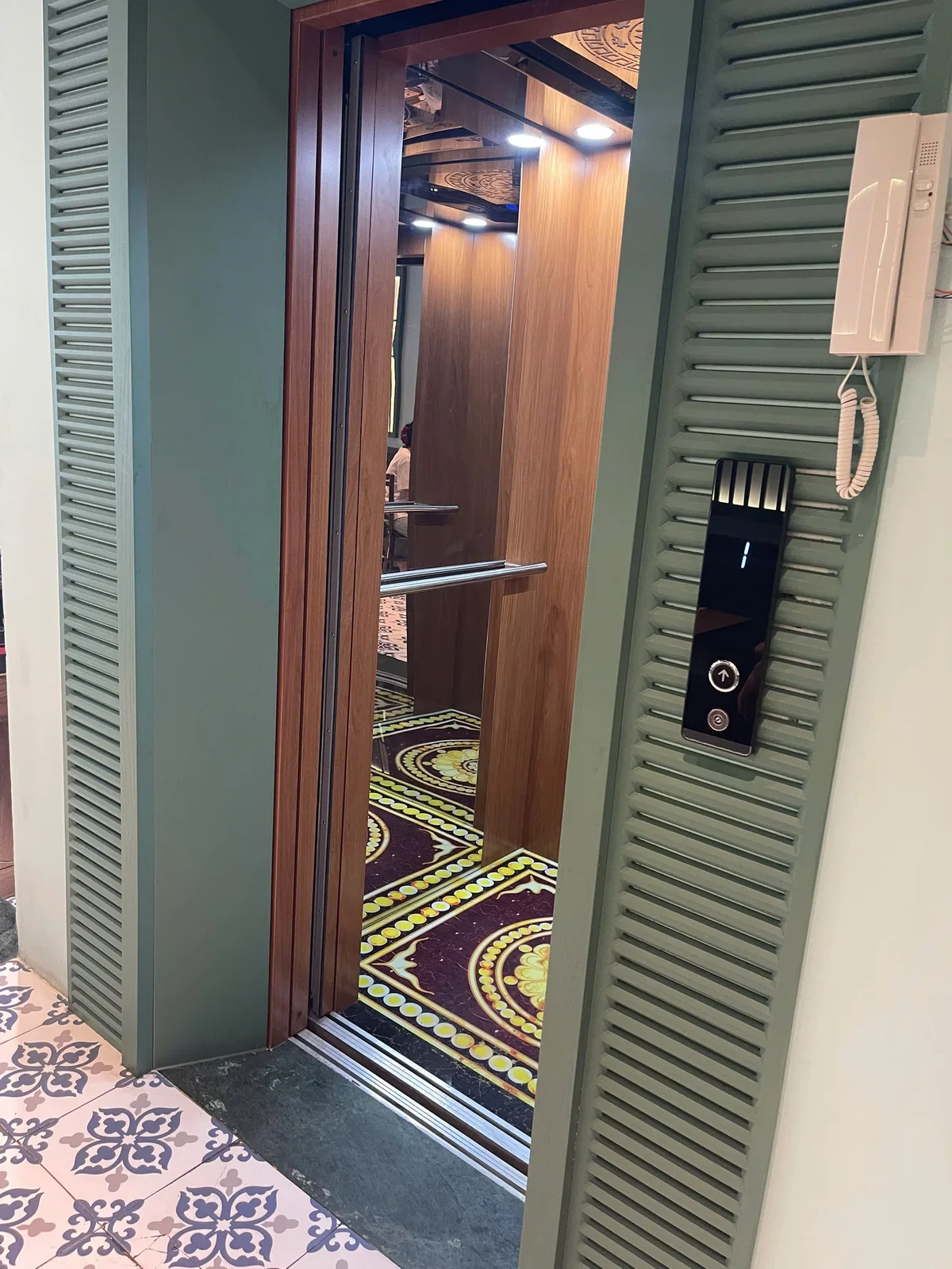 Cửa thang mở lộ cabin ốp gỗ, tay vịn và sàn hoa văn.