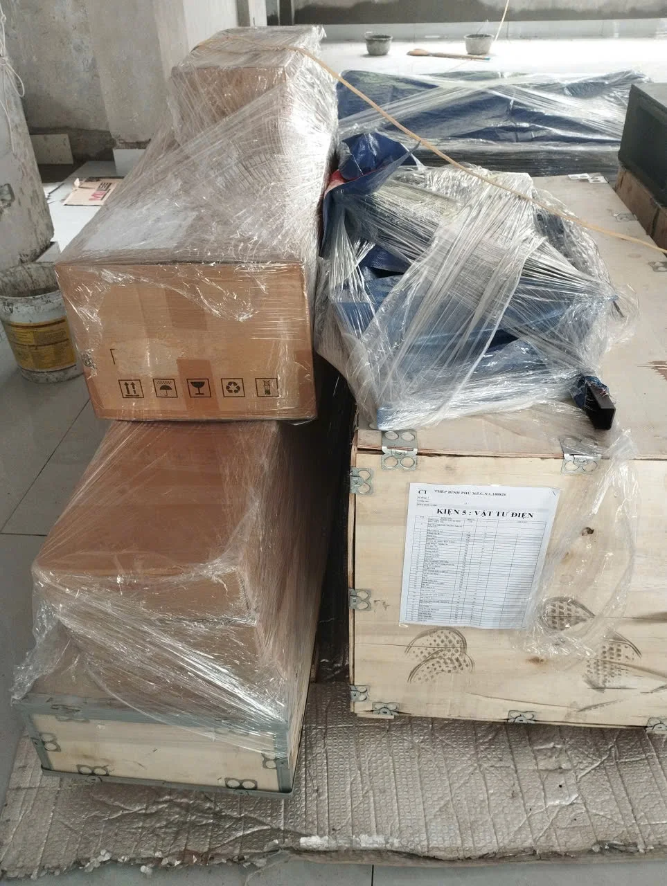 Kiện gỗ, hộp carton và các phần vật tư được bọc màng đặt cạnh nhau.
