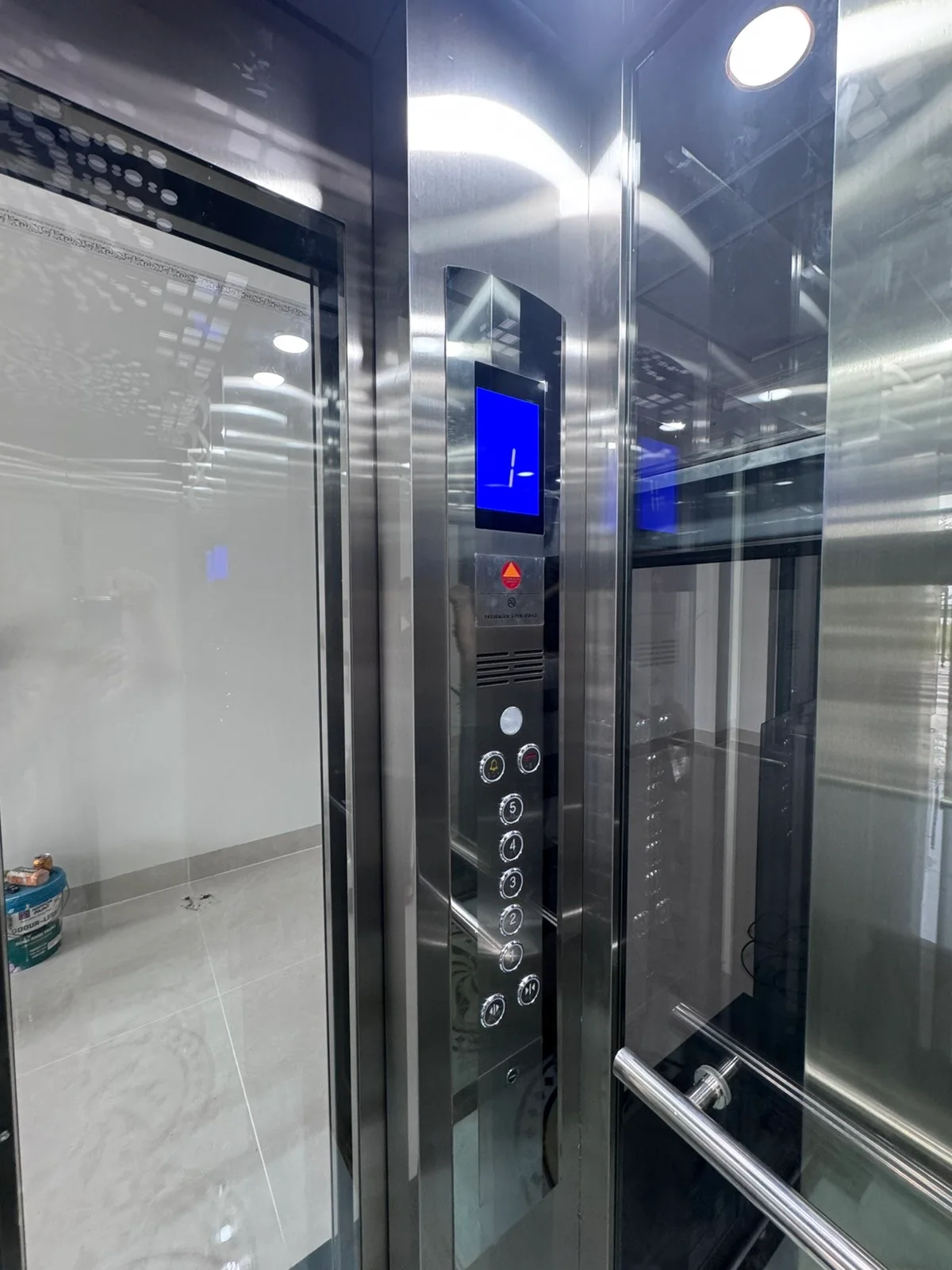 Bảng điều khiển cabin có màn hình xanh và dãy nút tròn trên vách inox.