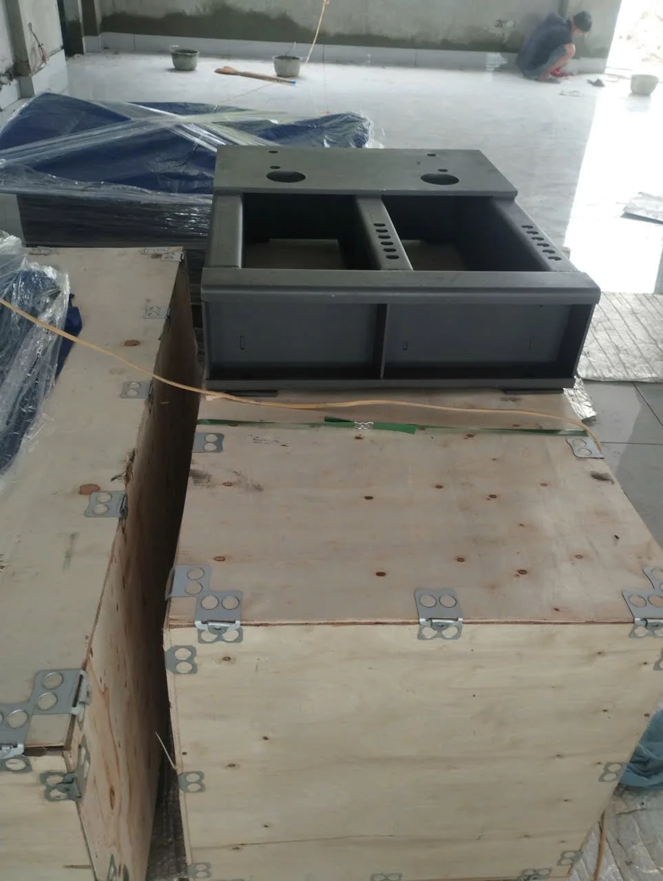 Cụm khung kim loại xám dạng hộp đặt trên kiện gỗ.