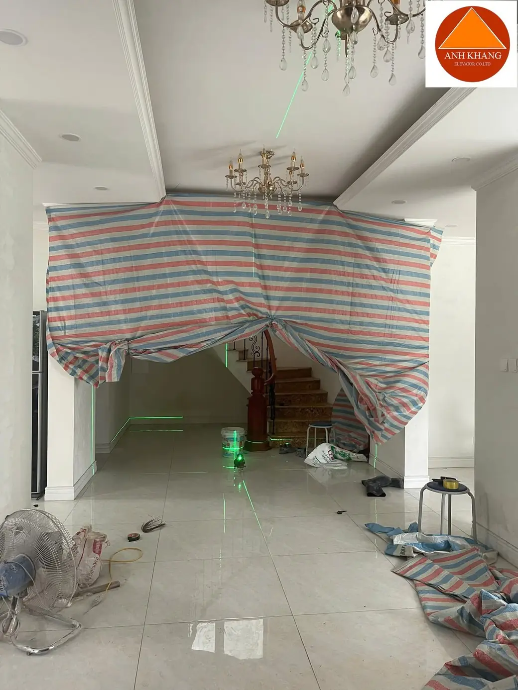 Bạt ngăn khu vực cầu thang trong nhà có sàn và trần đã hoàn thiện, dụng cụ thi công đặt trên sàn.